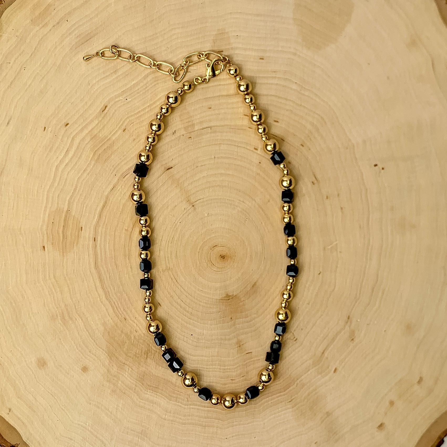This necklace has gold tone and black beads. It is placed against a wooden background.