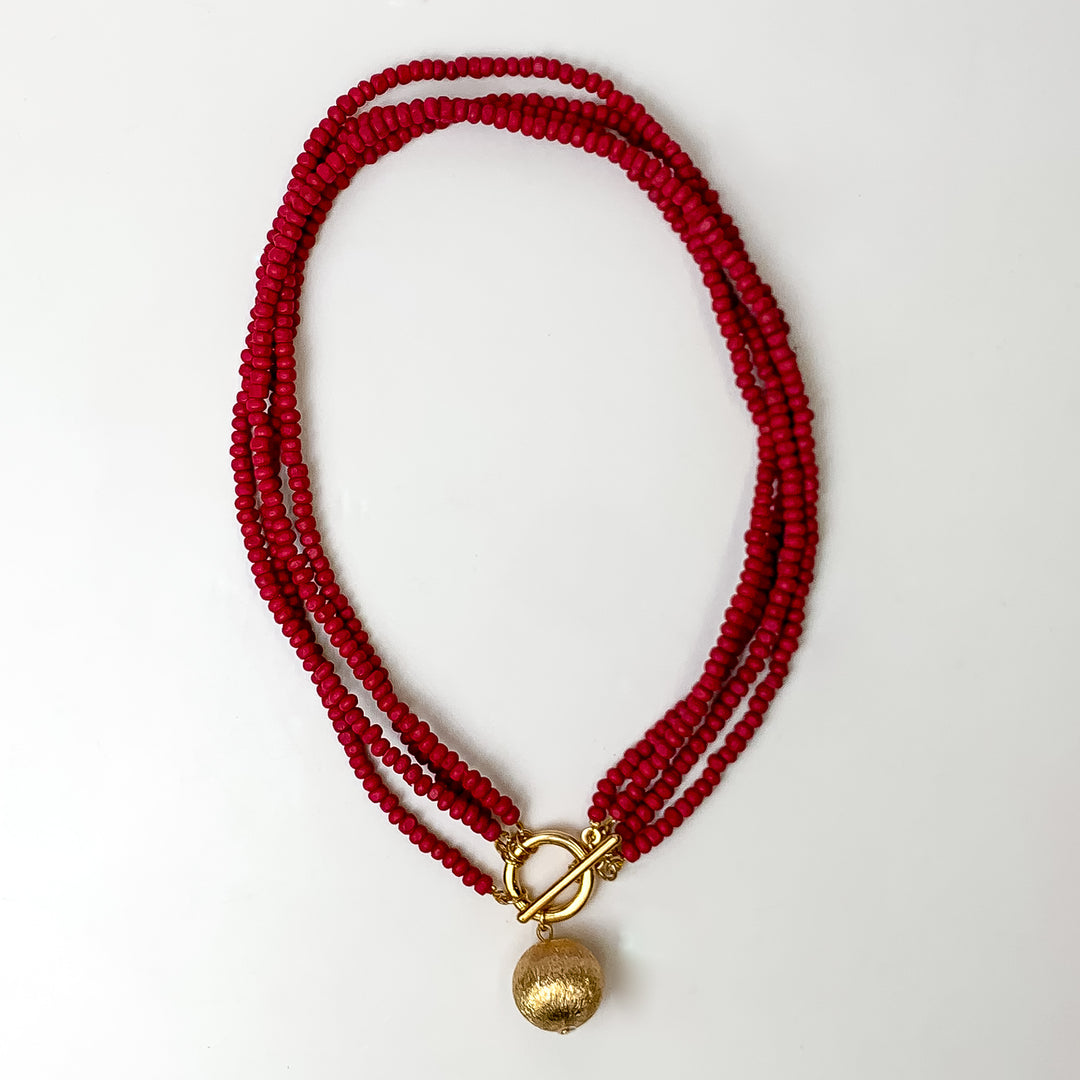 This beaded necklace has 4 strands and features a gold tone ball as the centerpiece. It is taken on a white background.