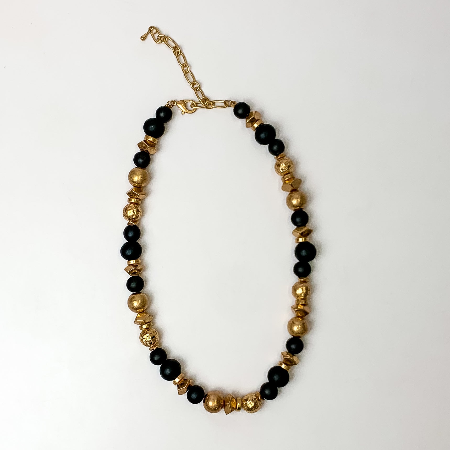 This texture beaded necklace with gold tone and black beads are placed on a white background.