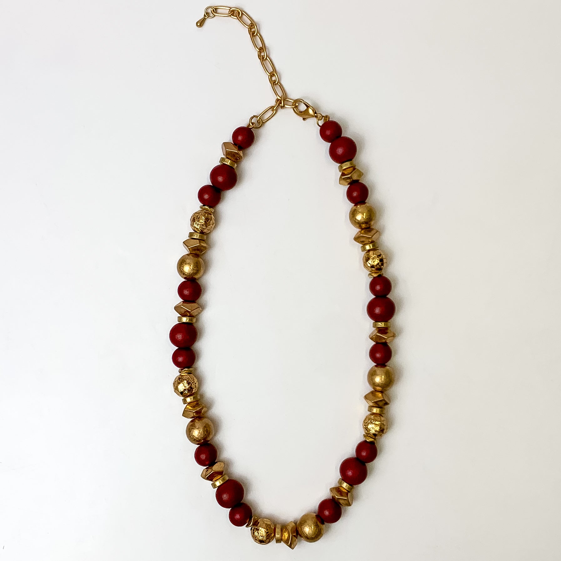 This texture beaded necklace with gold tone and maroon beads are placed on a white background.