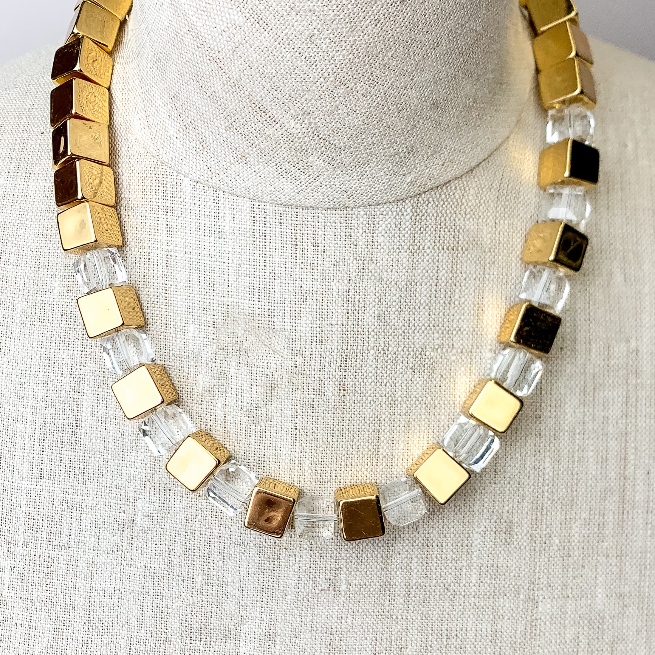 This Fashionably Late Gold Tone Cubed Necklace in Clear is pictured on an ivory mannequin with a white background.
