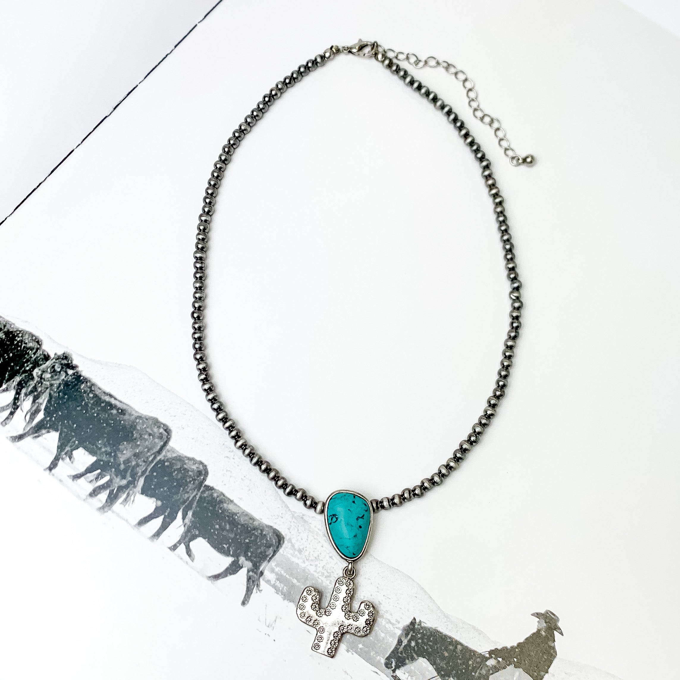 Cactus Queen Faux Navajo Silver Tone Necklace with Stone in Turquoise. Pictured on a white page with a cow scene printed on it.