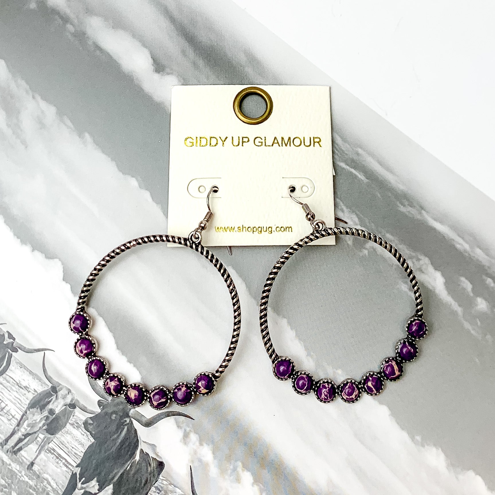Forever Twisted Hoop Earrings with Stones in Purple. Pictured on a book with a western background behind the earrings.