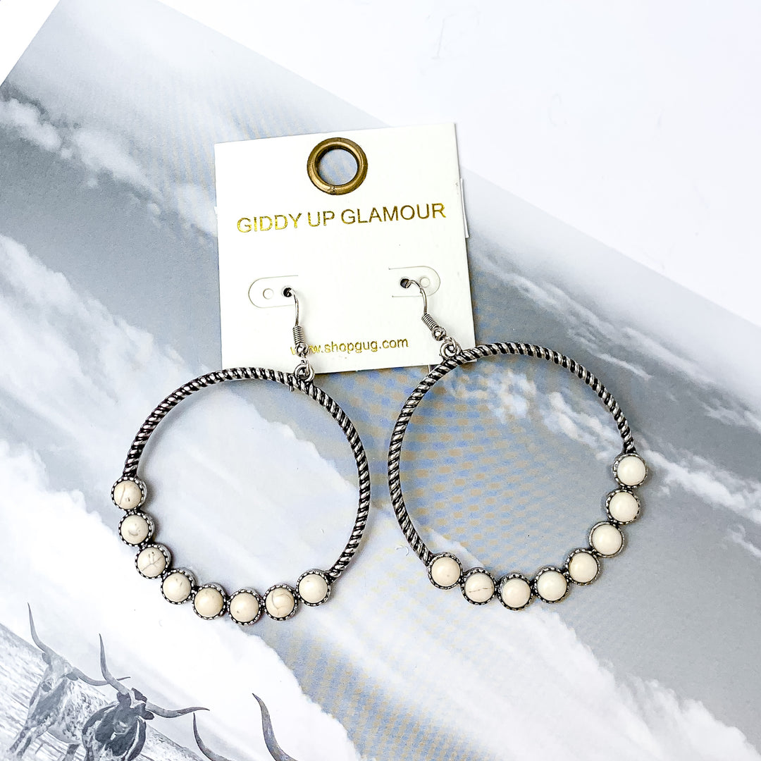 Forever Twisted Hoop Earrings with Stones in Ivory. Pictured on a white background with a western scene on the book behind the earrings. 