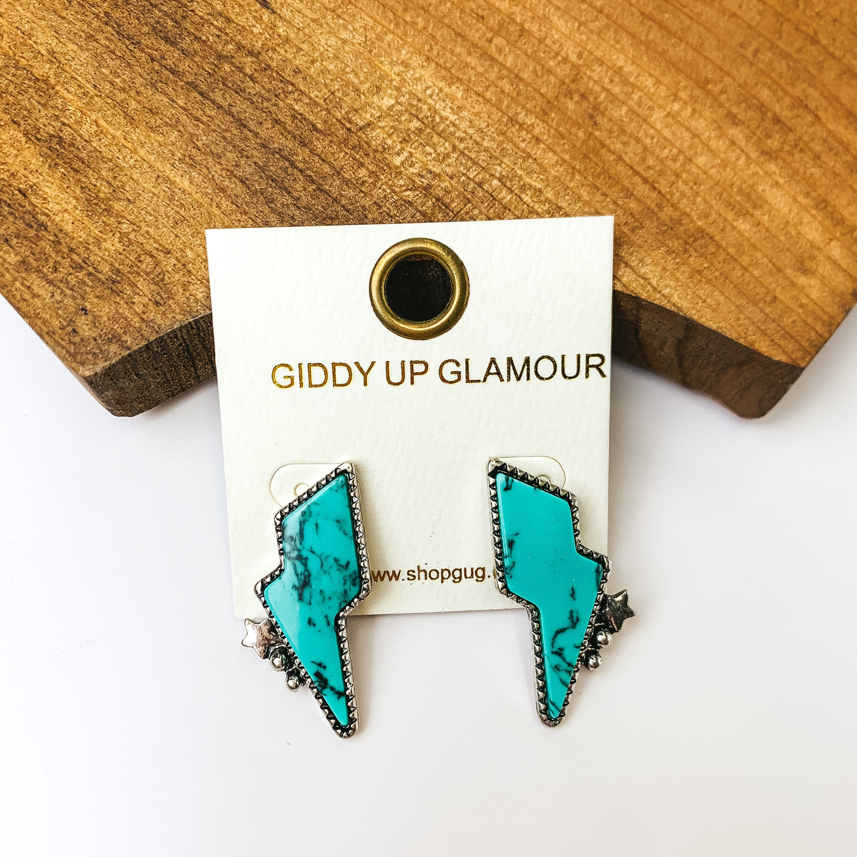 Driving Down Lightning Bolt Stone Post Earrings in Turquoise with Silver Detailing. Pictured on a white background with a wood piece behind it.