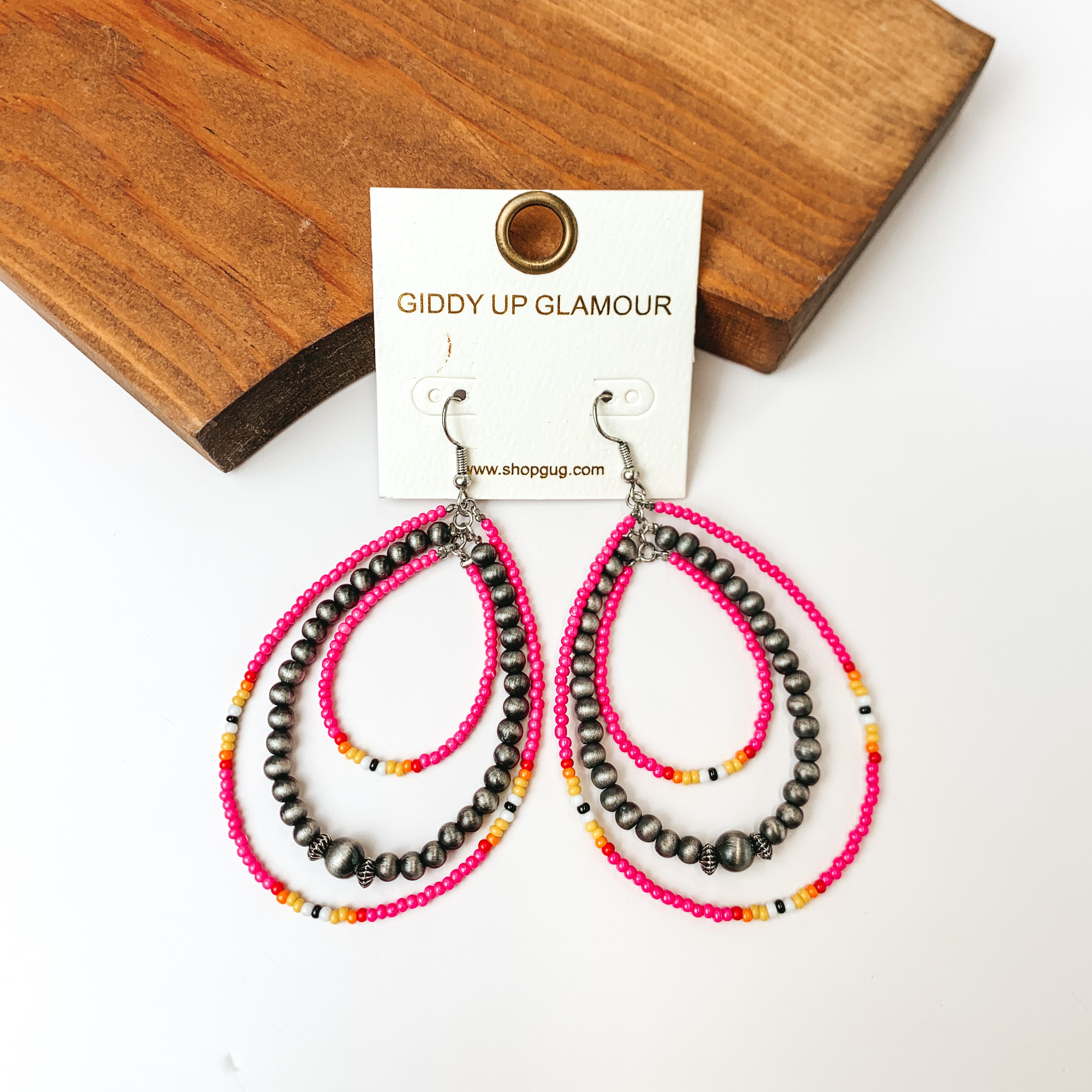 Western Style Triple Open Teardrop Earrings In Silver Tone and Hot Pink. Pictured on a white background with a piece of wood behind the earrings. 