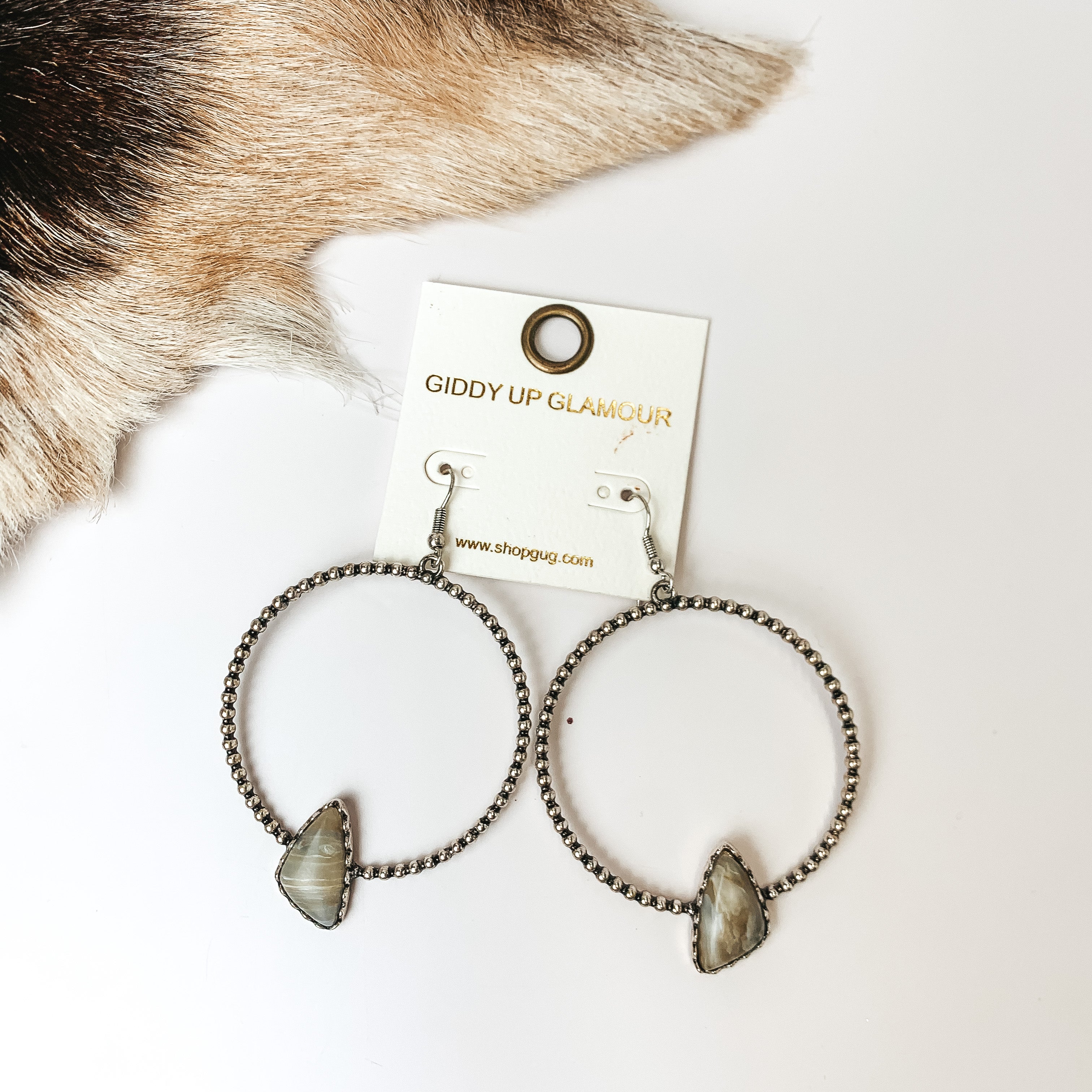 Silver Tone Textured Hoop Earring with Natural Stone. Pictured on a white background with faux animal fur to the top right. 
