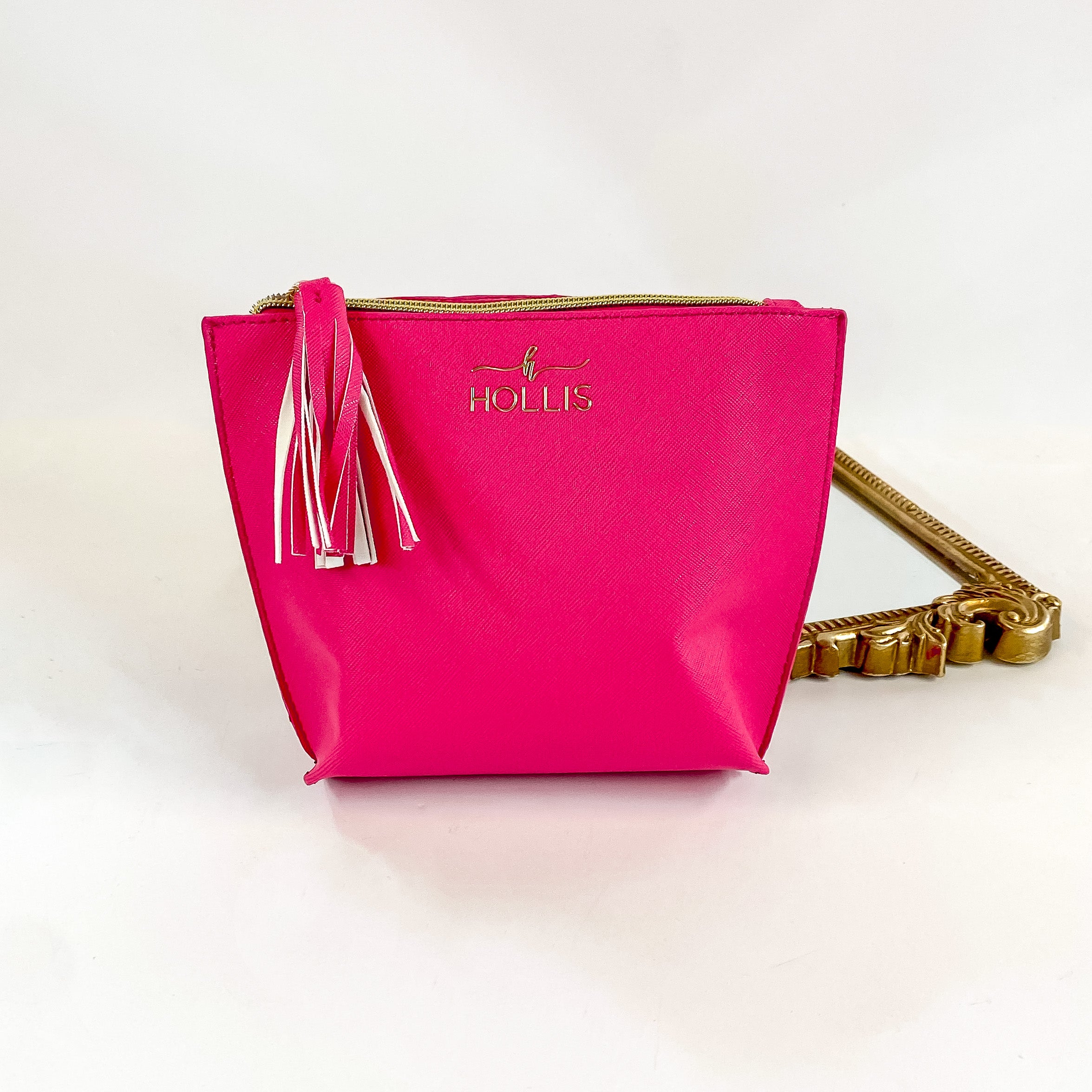 Smaller sized hot pink zip up bag with tassel charm Pictured on a white background with a mirror behind. 