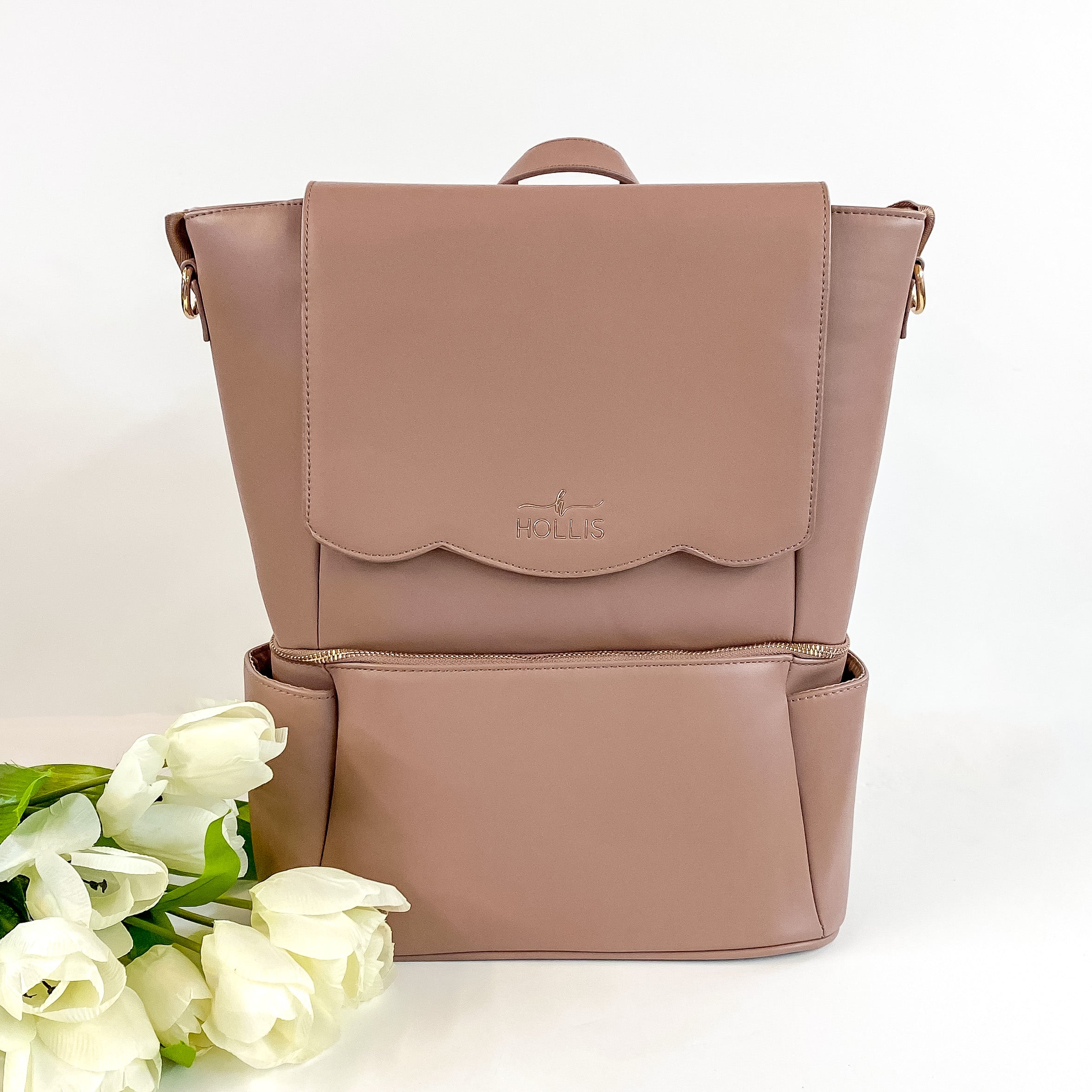 Hollis brand Diaper bag in metallic mocha. Has multiple departments and zippers. Pictured on a white background with roses in the bottom left corner. 