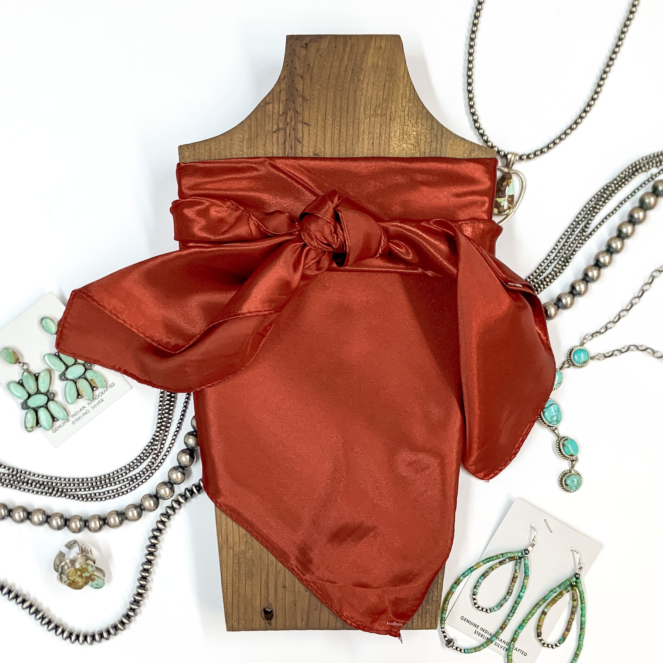 Solid colored scarf in Rust. Scarf is tied around a wooden piece. The scarf and piece of wood is pictured on a white background with Navajo jewelry spread out around it.