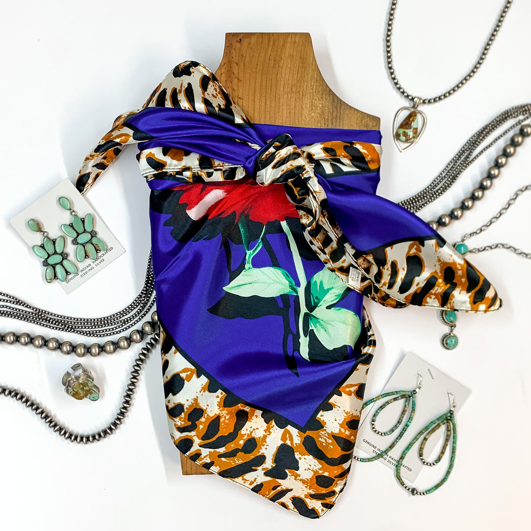Patterned scarf in Fiesty Floral royal blue. Scarf is tied around a wooden piece. The scarf and piece of wood is pictured on a white background with Navajo jewelry spread out around it.