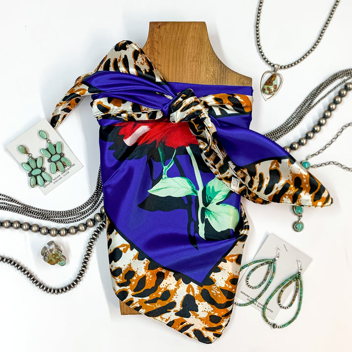 Patterned scarf in Fiesty Floral royal blue. Scarf is tied around a wooden piece. The scarf and piece of wood is pictured on a white background with Navajo jewelry spread out around it.