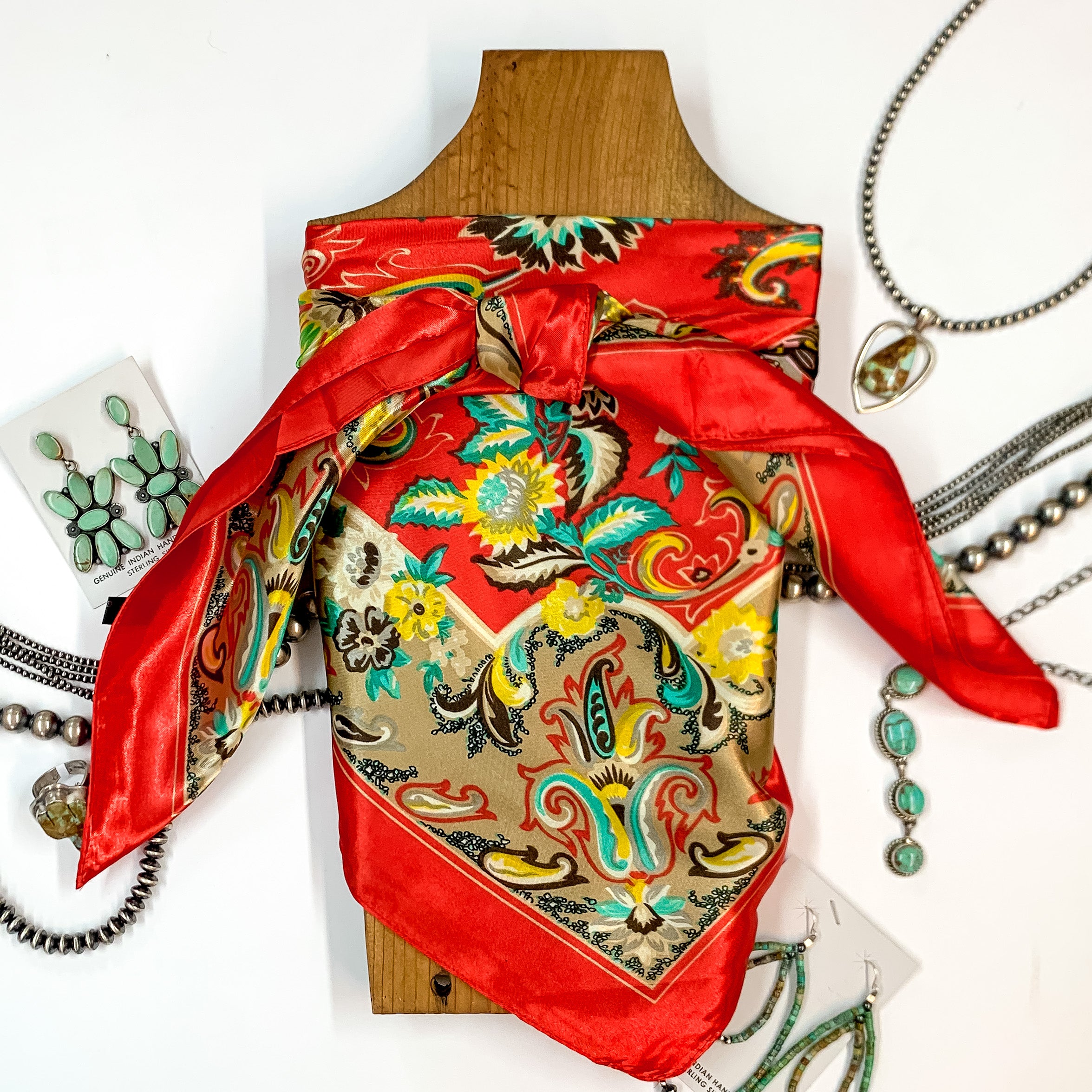Patterned scarf in Concho River. Scarf is tied around a wooden piece. The scarf and piece of wood is pictured on a white background with Navajo jewelry spread out around it.