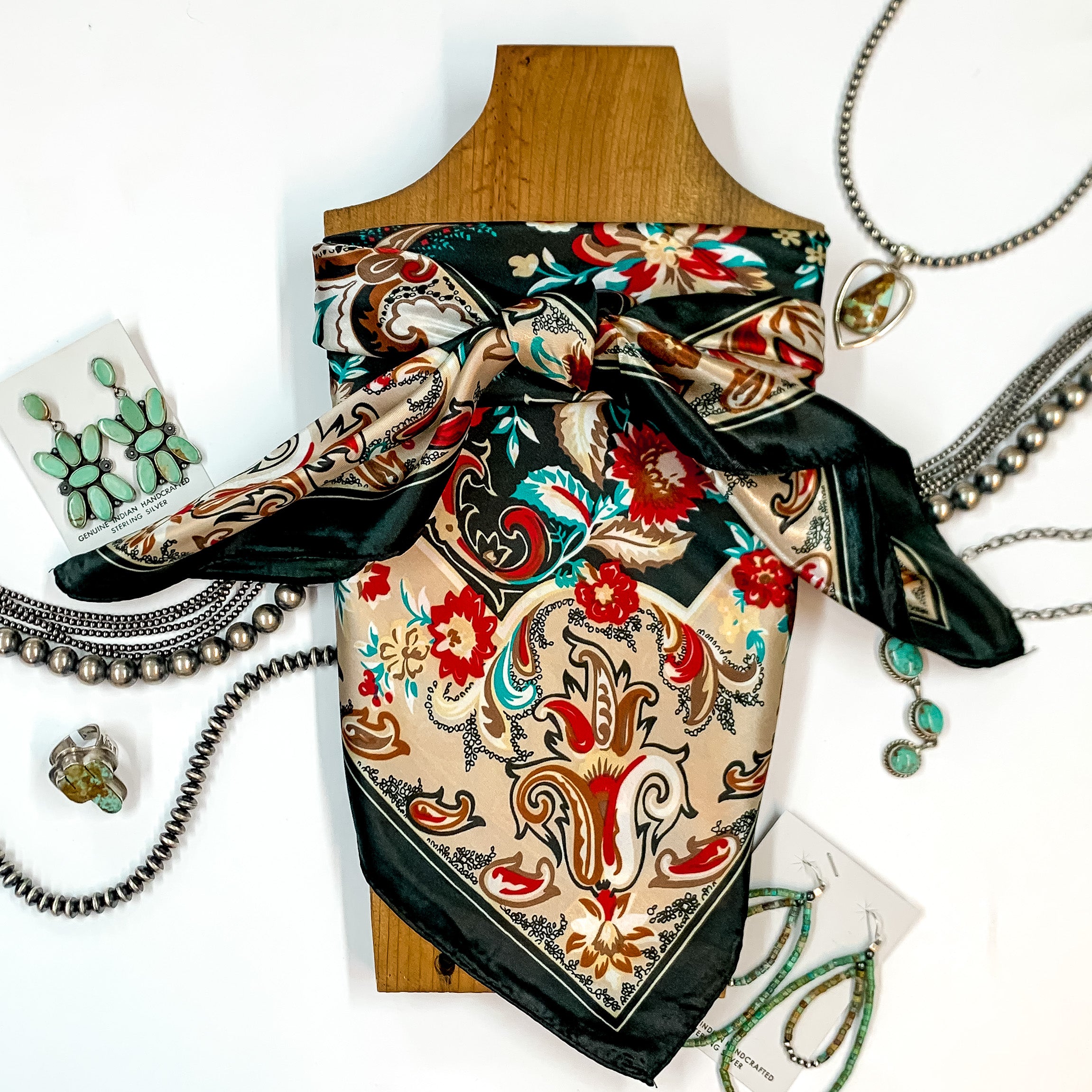 Patterned scarf in Quail Creek. Scarf is tied around a wooden piece. The scarf and piece of wood is pictured on a white background with Navajo jewelry spread out around it.
