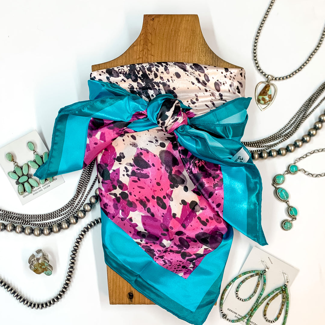 Patterned scarf in Cool Cowhide. Scarf is tied around a wooden piece. The scarf and piece of wood is pictured on a white background with Navajo jewelry spread out around it.