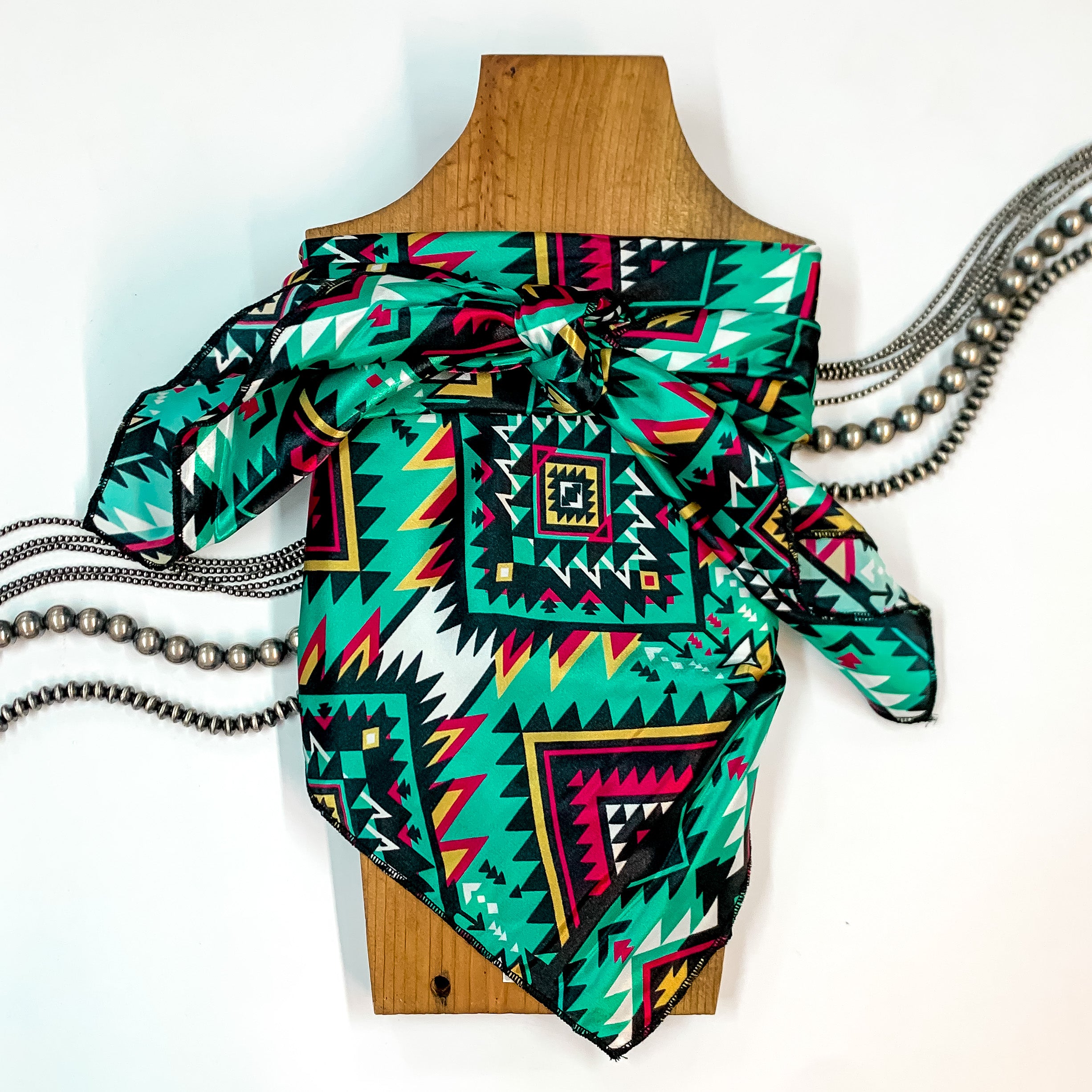 Patterned scarf in Santa Fe. Scarf is tied around a wooden piece. The scarf and piece of wood is pictured on a white background with Navajo jewelry spread out around it.