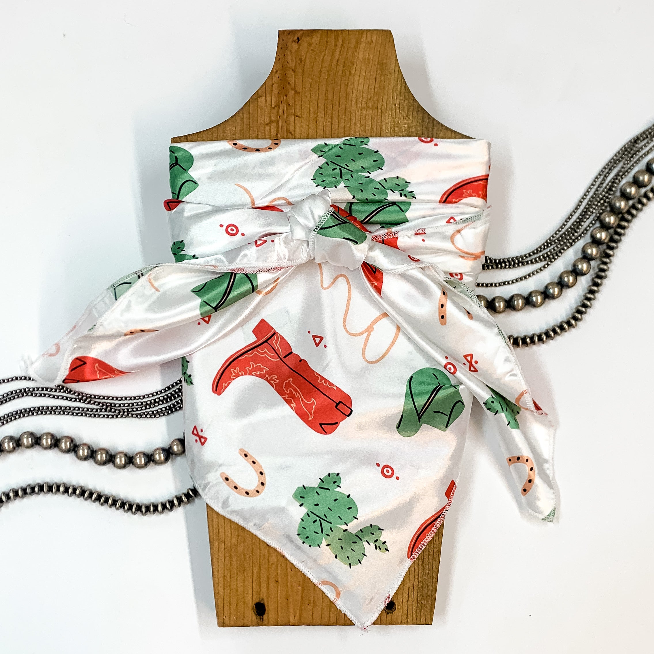 Patterned scarf in Boozy Boot. Scarf is tied around a wooden piece. The scarf and piece of wood is pictured on a white background with Navajo jewelry spread out around it.