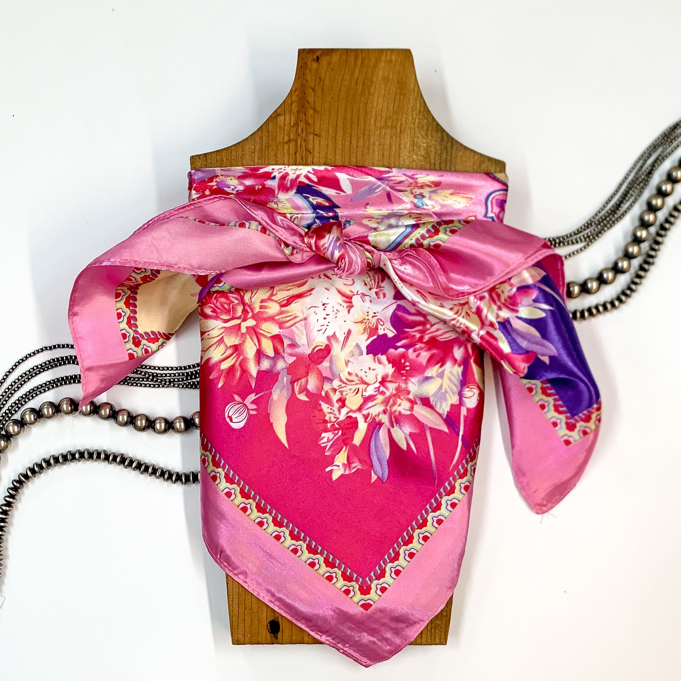 Patterned scarf in Desert Petals. Scarf is tied around a wooden piece. The scarf and piece of wood is pictured on a white background with Navajo jewelry spread out around it.