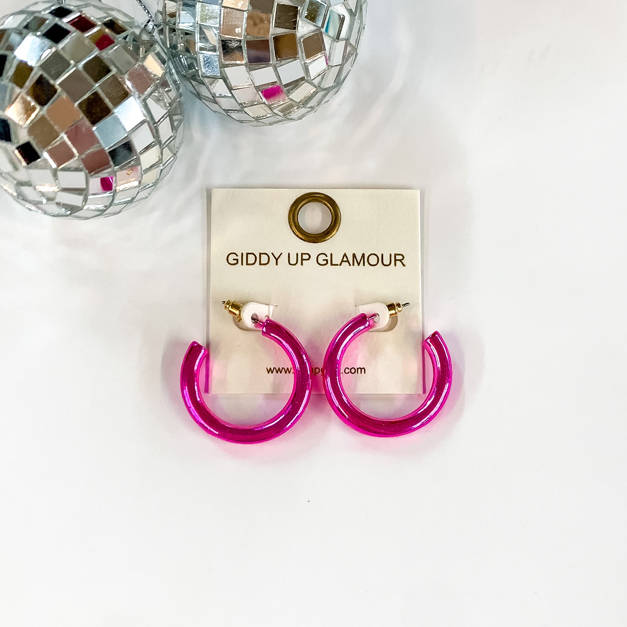 Light up Small Neon Hoop Earrings in Hot Pink. Pictured on a white background with disco balls in the top left corner.