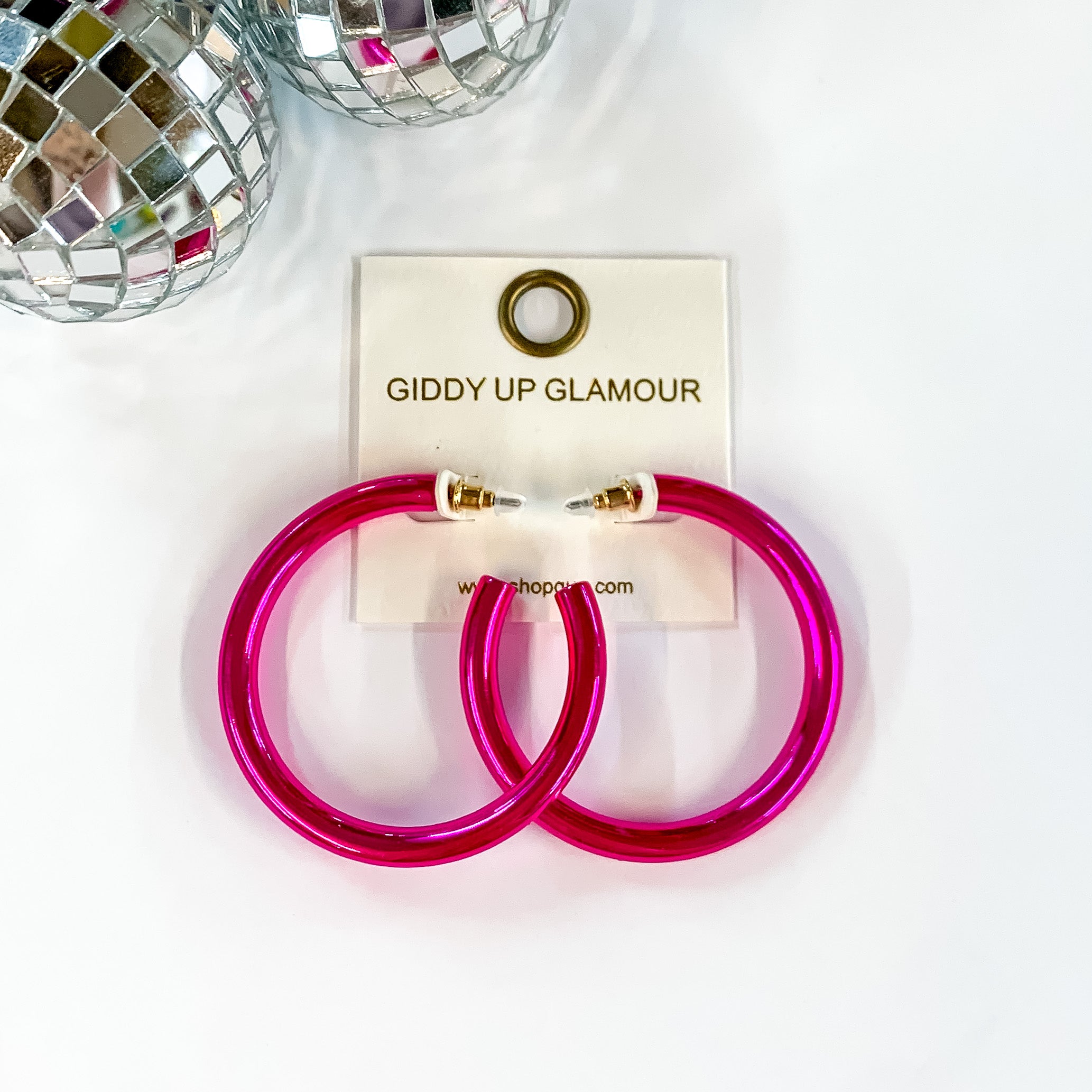 Light up Large Neon Hoop Earrings in Hot Pink. Pictured on a white background with disco balls in the top left corner.