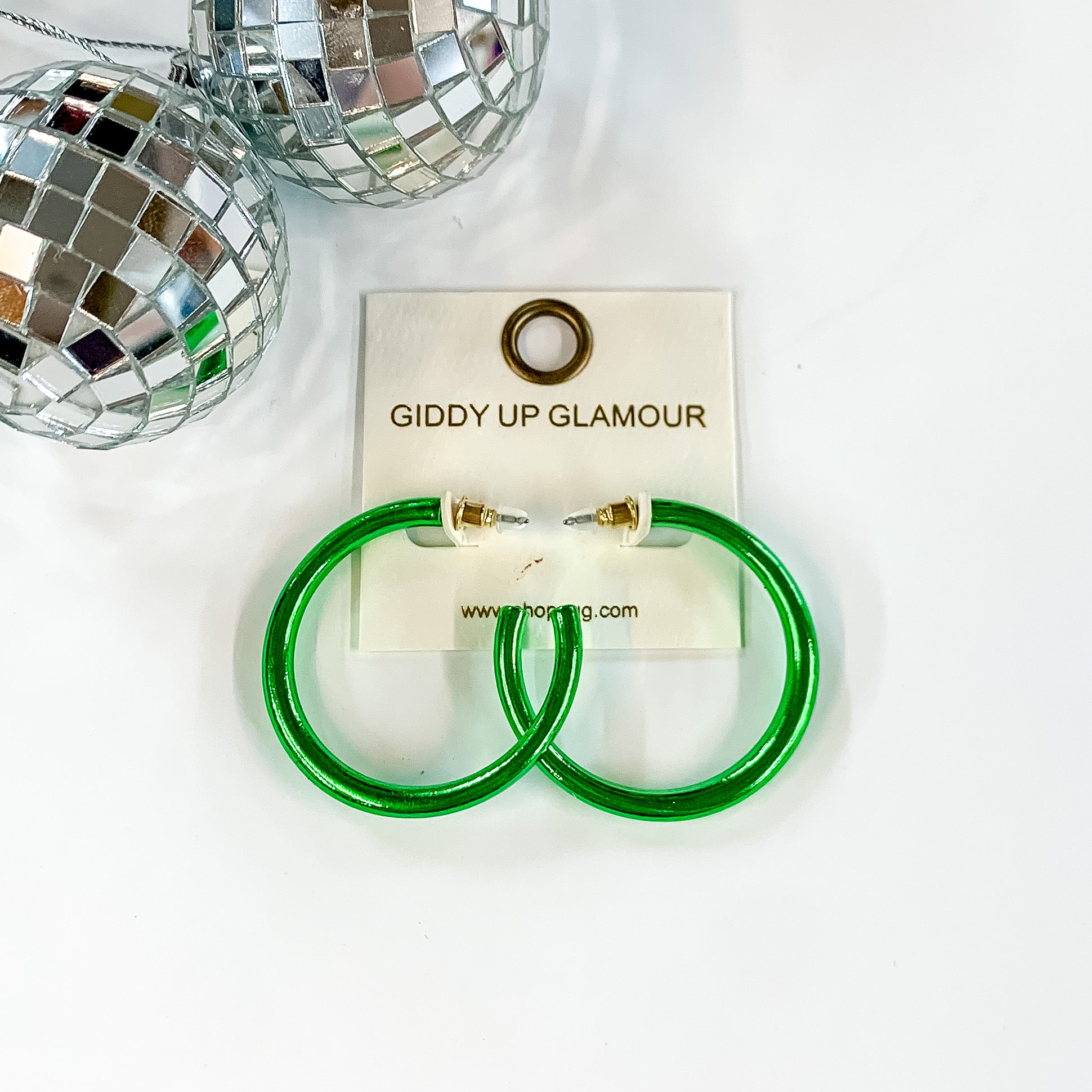 Light Up Medium Neon Hoop Earrings In Green. Pictured on a white background with disco balls in the top left corner.