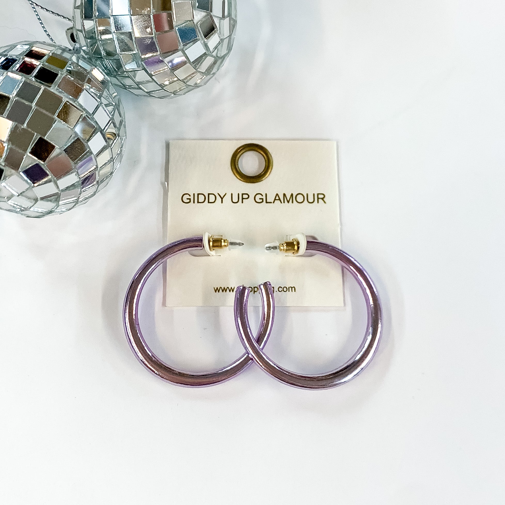Light Up Medium Neon Hoop Earrings In Lavender. Pictured on a white background with disco balls in the top left corner.