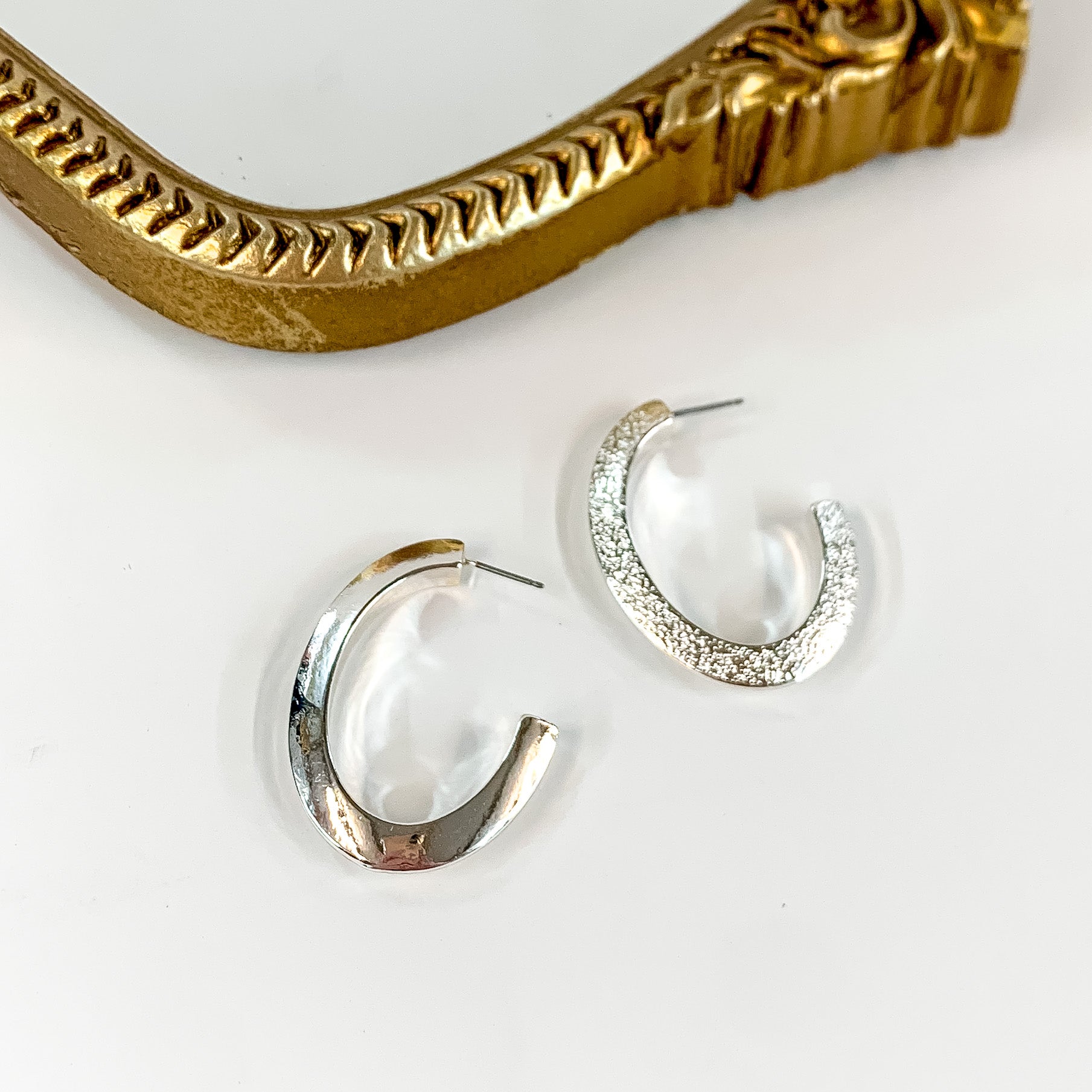 Thick Oval Silver Tone Hoop Earrings. Pictured on a white background with a gold frame at the top.