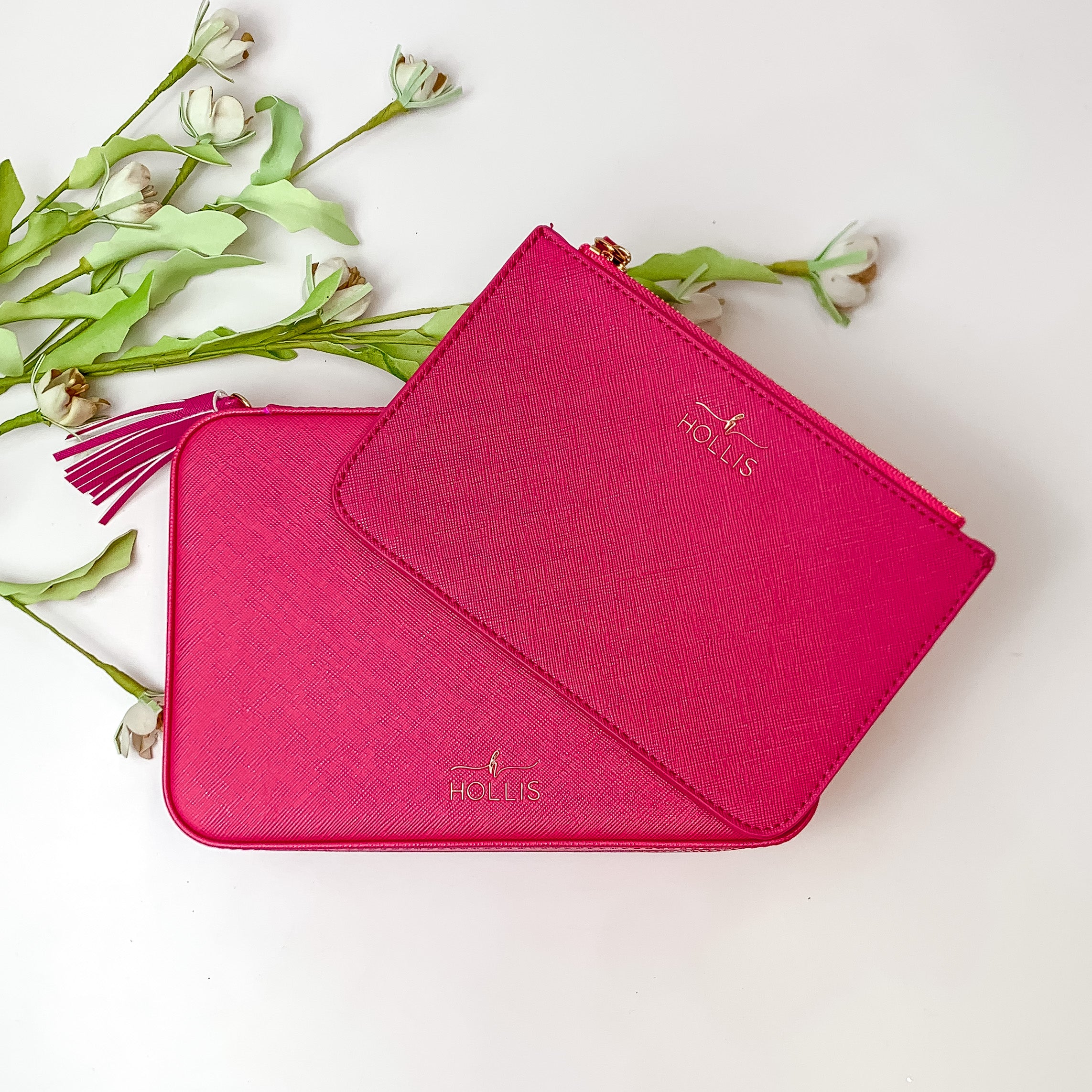 Two hot pink jewelry totes pictured on top of each other. These bags are pictured on a white background with green and white flowers in the background. 