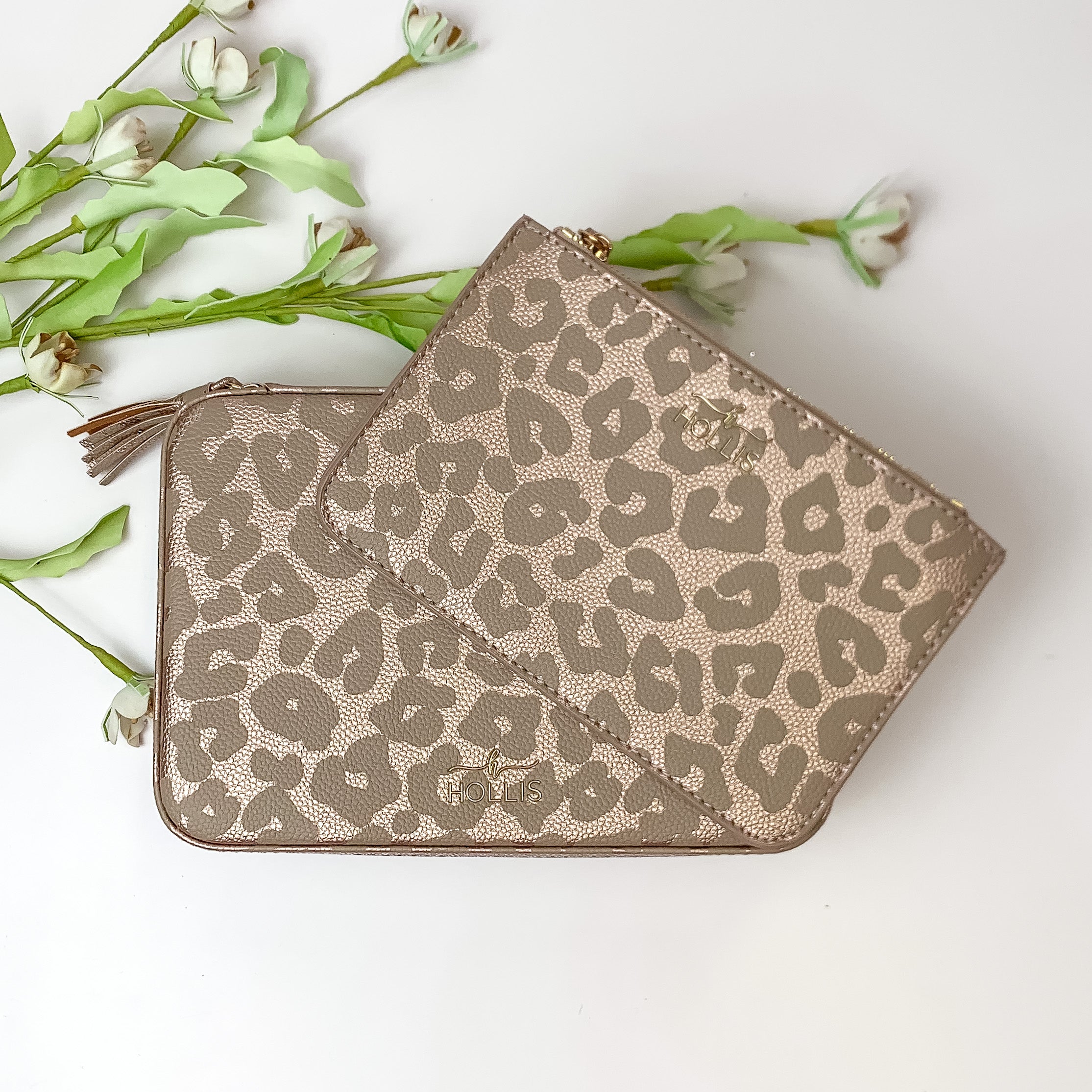 Light brown metallic leopard jewelry totes pictured on top of each other. These bags are pictured on a white background with green and white flowers in the background. 