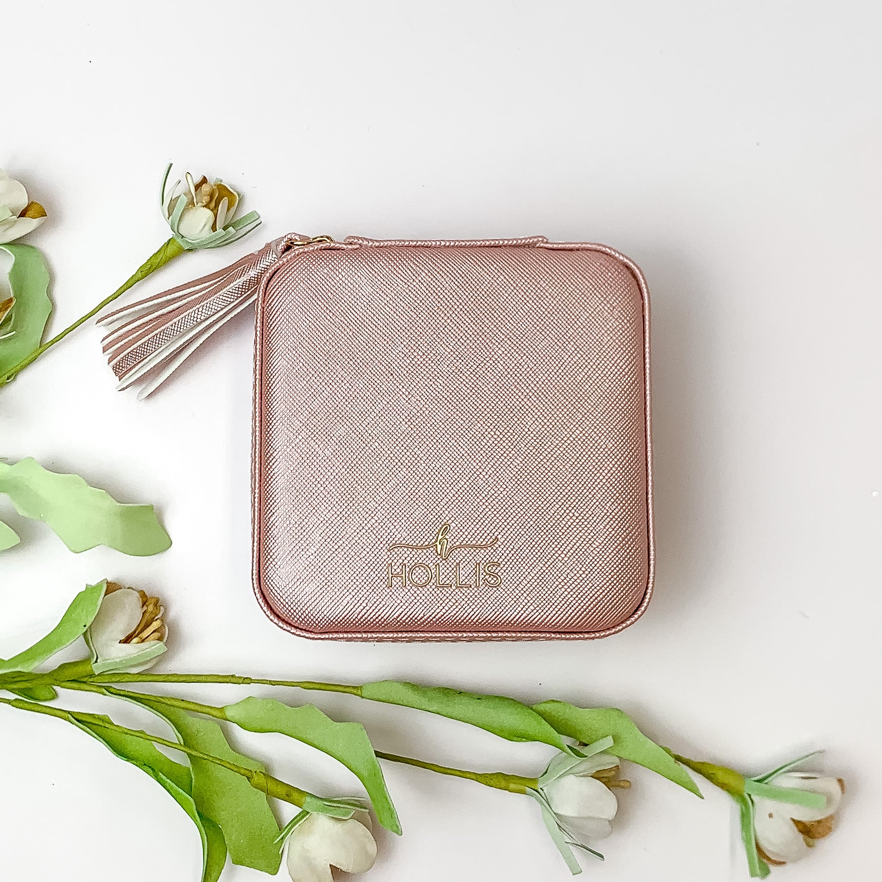Blush jewelry box pictured on a white background with green and white flowers in the background. 