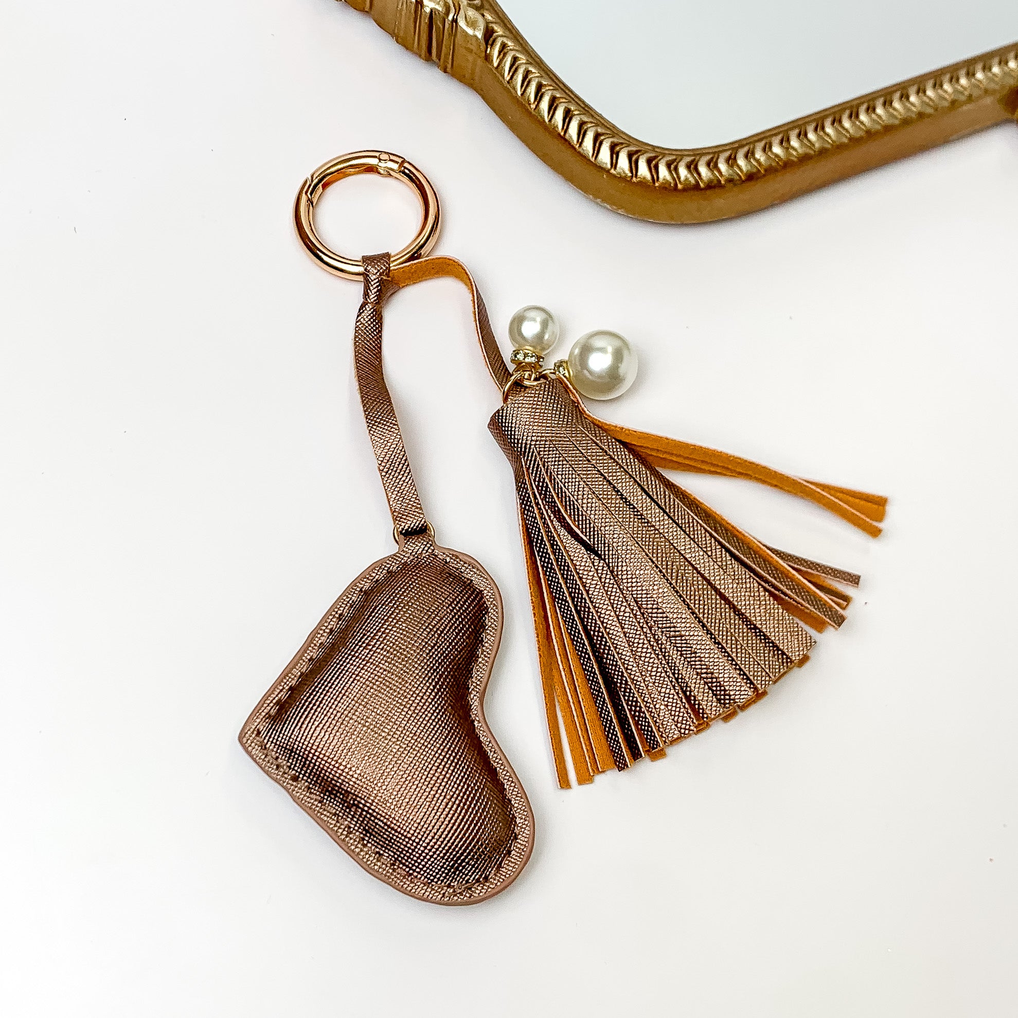 Gold key ring with a metallic mocha tassel and heart charm. The tassel includes two white, pearl beads. This keychain is pictured on a white background. 