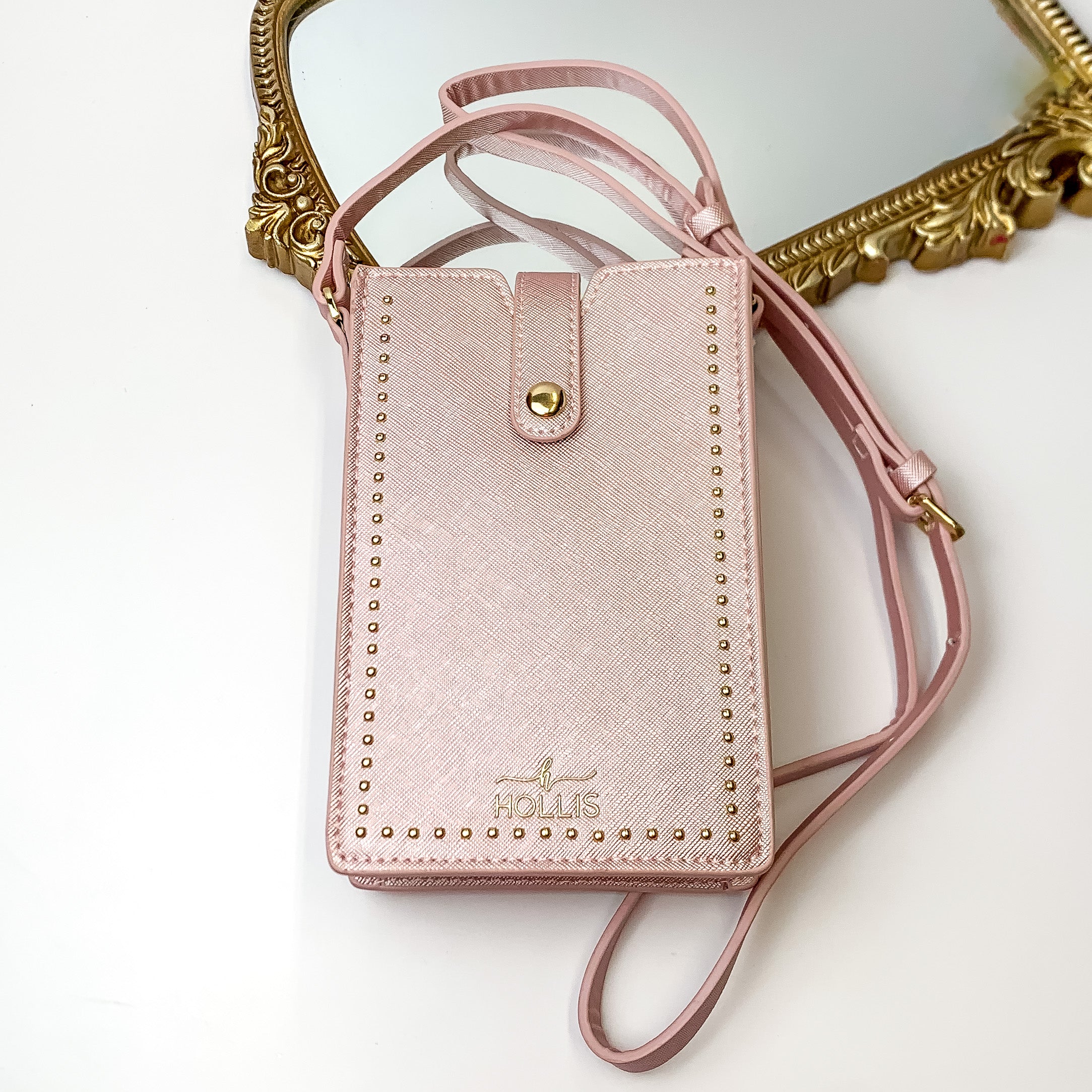 Metallic blush, rectangle purse with gold studs pictured in front of a gold mirror on a white background. 