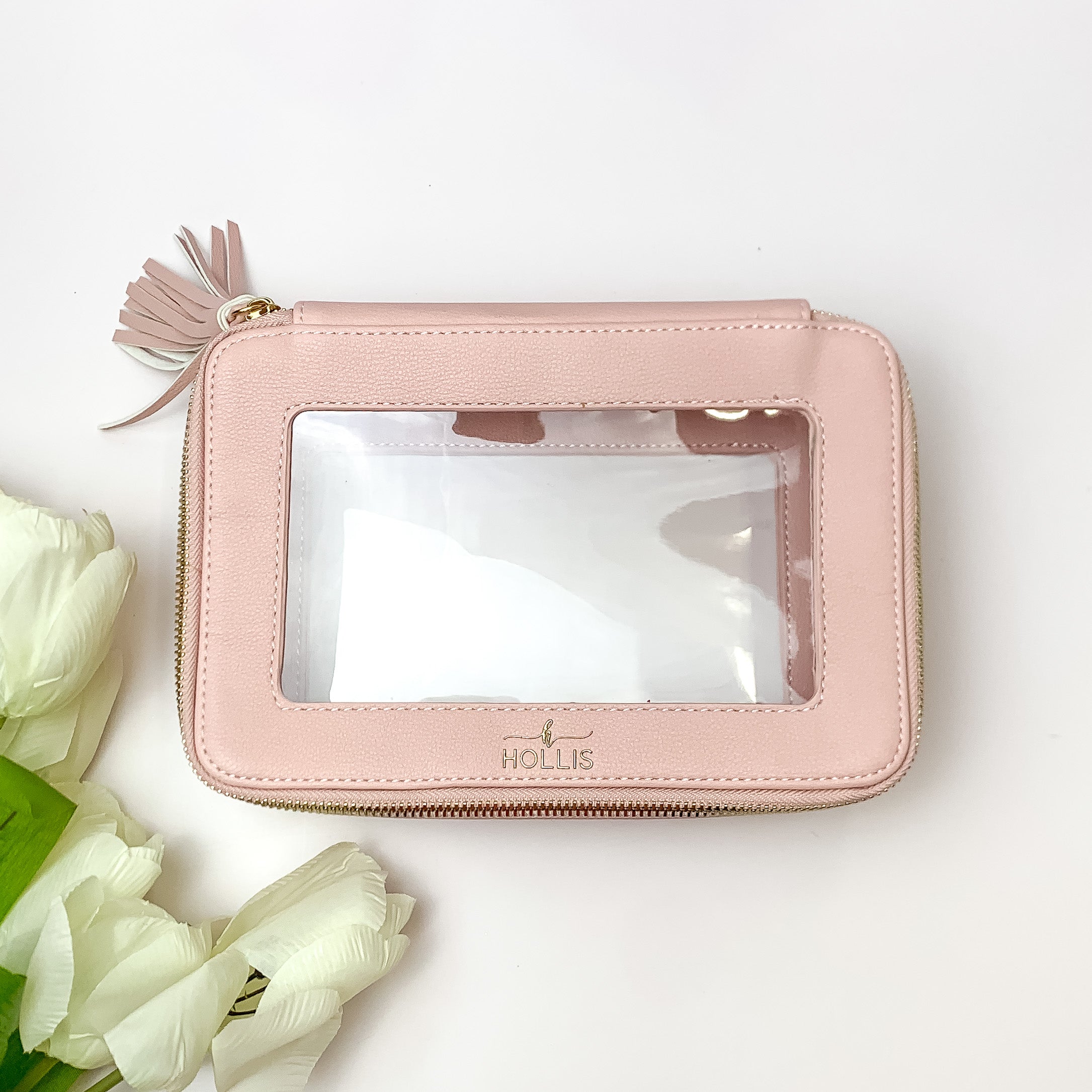 Blush pink and clear rectangle toiletry bag pictured on a white background with white flowers on the bottom left corner. 