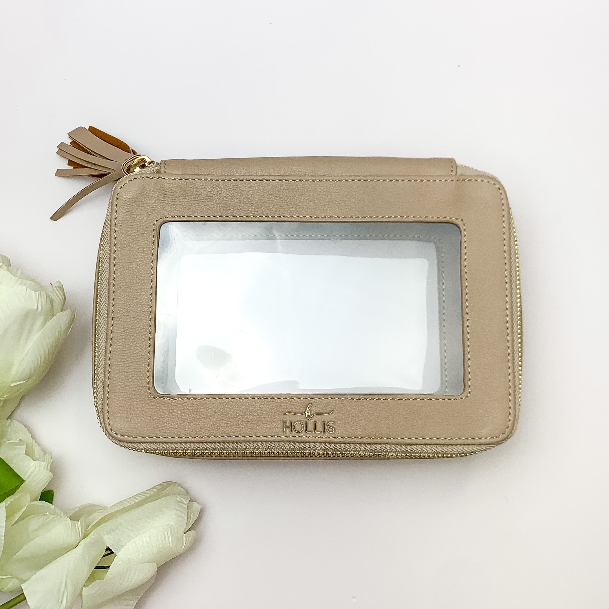 Nude and clear rectangle toiletry bag pictured on a white background with white flowers on the bottom left corner. 