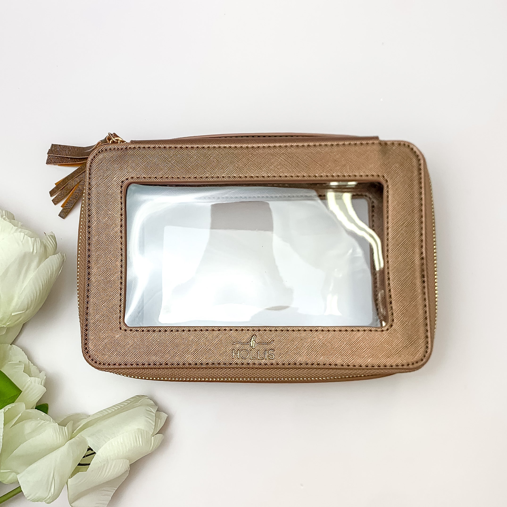 Metallic mocha and clear rectangle toiletry bag pictured on a white background with white flowers on the bottom left corner. 