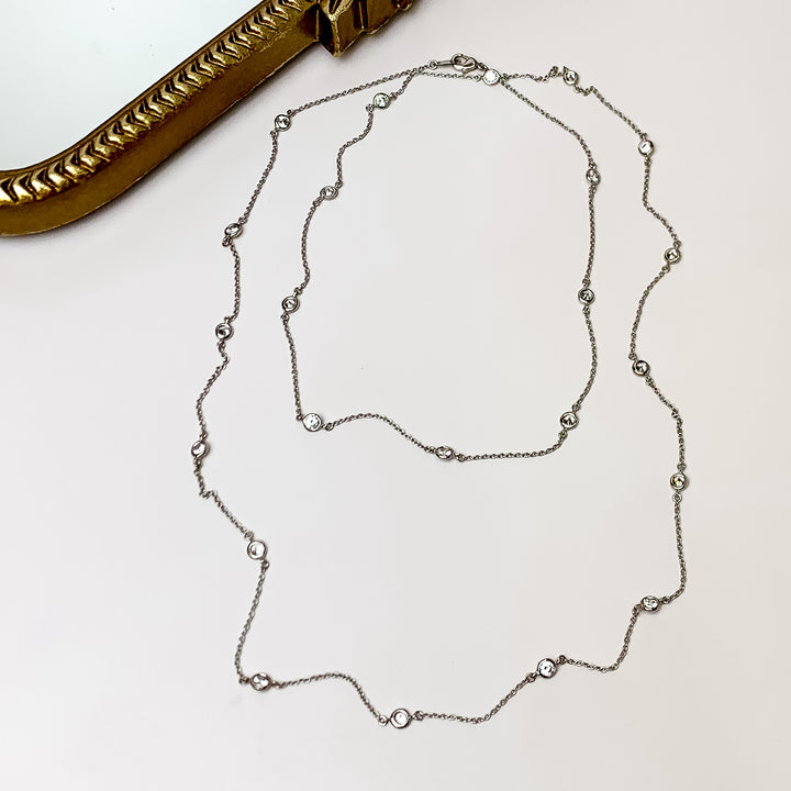 Simple Long Silver Tone Necklace With Clear Crystals. Pictured on a silver background with a piece of wood behind the necklace.