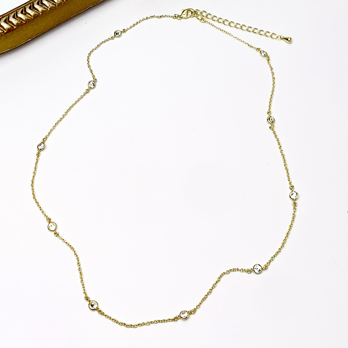 Simple Gold Tone Necklace With Clear Crystals. Pictured on a white background with a gold frame in the top left corner.