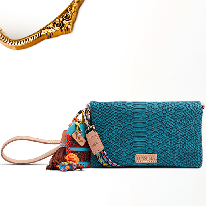 A gold mirror decal on a white background featuring Indy Uptown Crossbody features a turquoise, reptile-inspired texture, natural leather trim, and thoughtful details like the Jody charm and leather tag. With double magnetic closure, two interior zipper compartments, an exterior zip pocket, and both a detachable wristlet and adjustable woven crossbody strap, it’s as functional as it is fabulous.