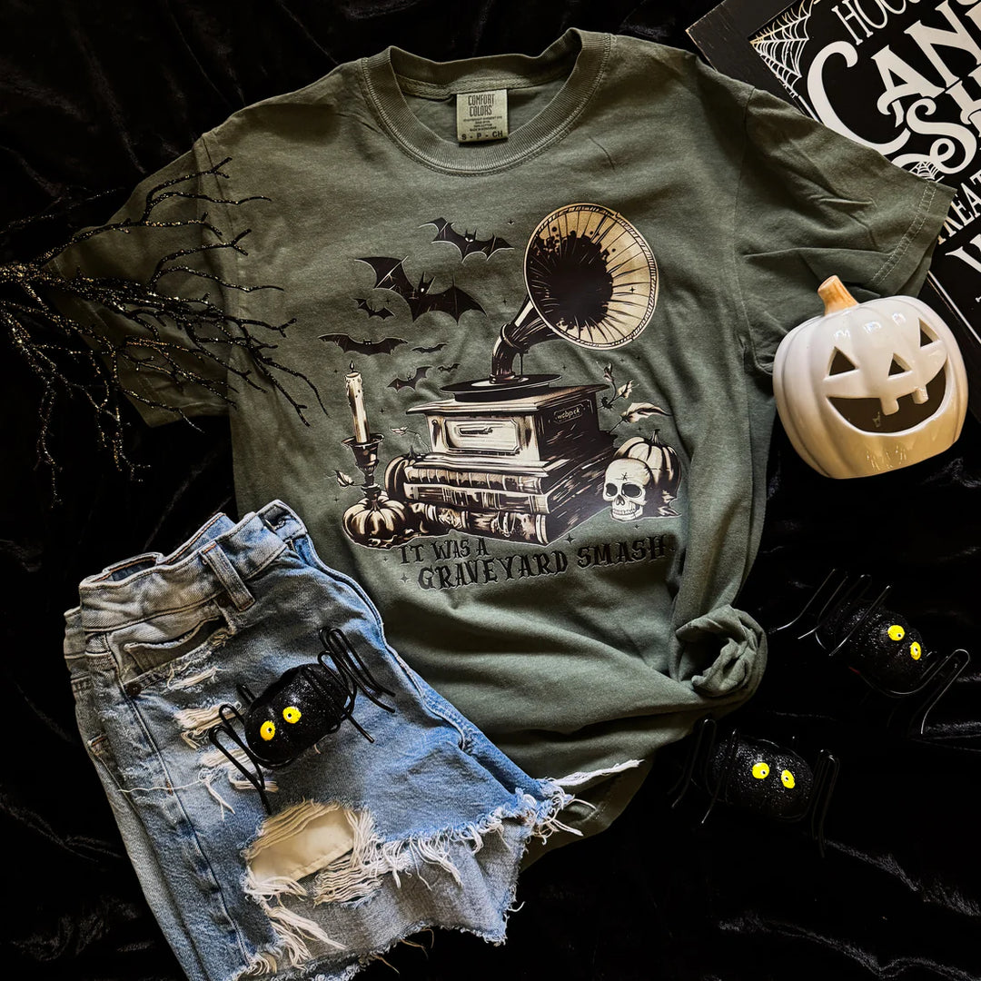 Green t-shirt with Halloween design featuring a gramophone and text, paired with denim shorts on a dark background.