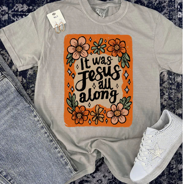 Gray t-shirt with 'It was Jesus all along' design on an orange background, next to jeans and a white sneaker.