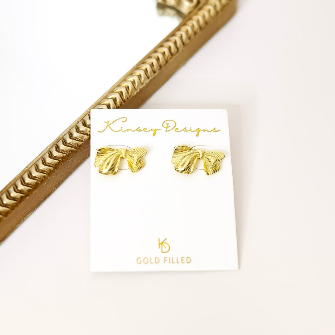 Gold bow earrings on a Kinsey Designs card with a gold frame in the background
