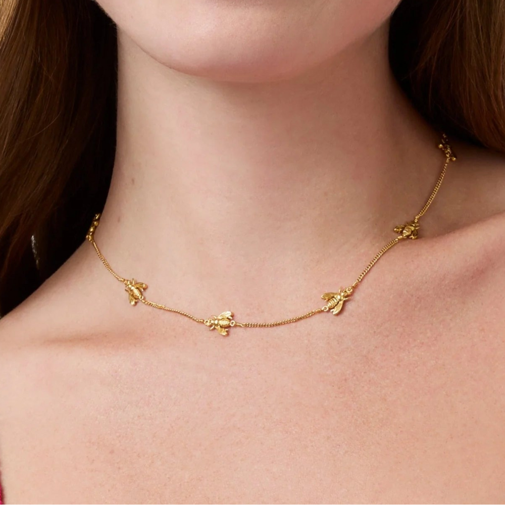 Woman wearing a gold bee necklace with a plain background
