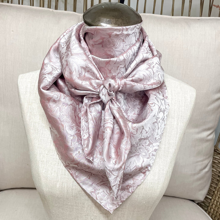 a blush colored wild rag with a jacquard print, tired around a mannequin neck.