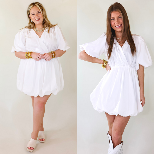 A short white babydoll dress featuring a V neck line, puffed sleeves, pleated top and skirt, and a puffed skirt.