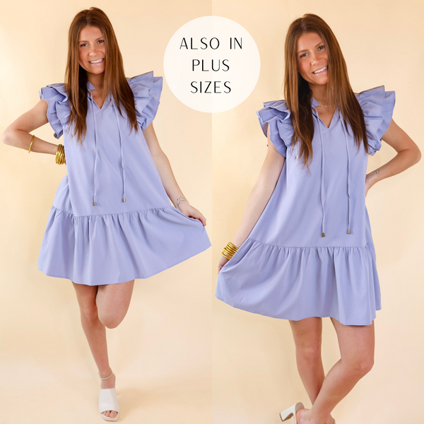A relaxed fit mini dress in the color periwinkle. Features a unique tieable keyhole neckline, short ruffled sleeves, and a ruffled hem. Item is pictured on a pale pink background