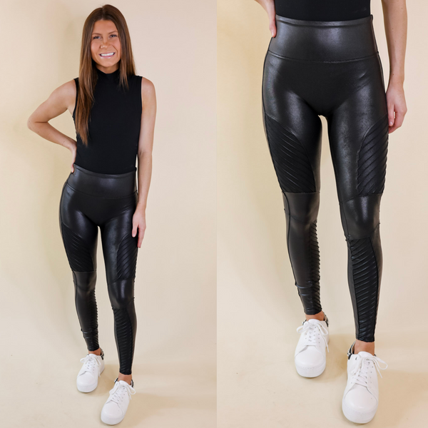 Model is wearing a pair of high waist faux leather leggings with moto detailing on the legs. Model has these leggings paired with a black tank top and white sneakers.