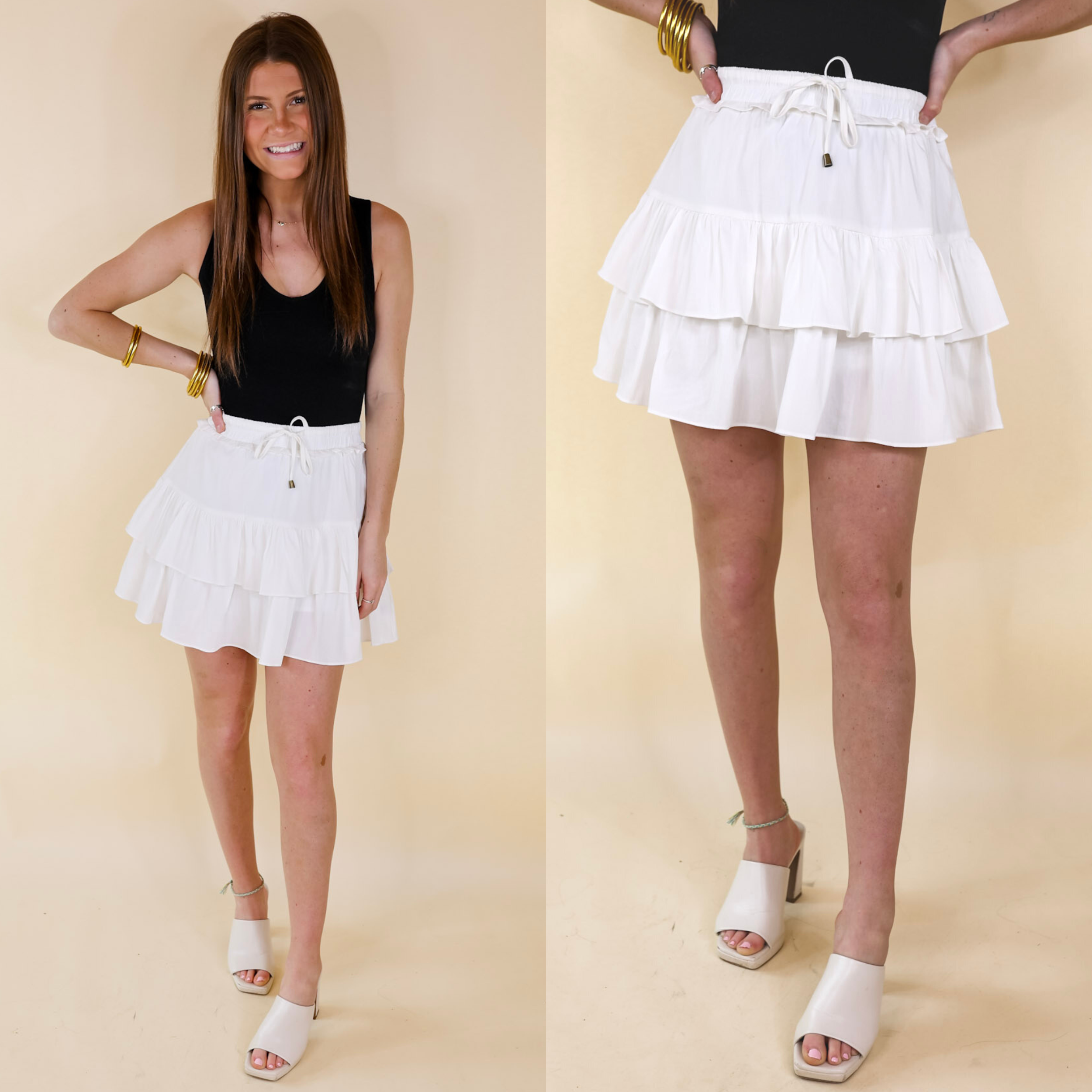 Model is wearing a ruffle tiered skort in off white. Model has it paired with ivory heels, a black bodysuit, and gold jewelry.
