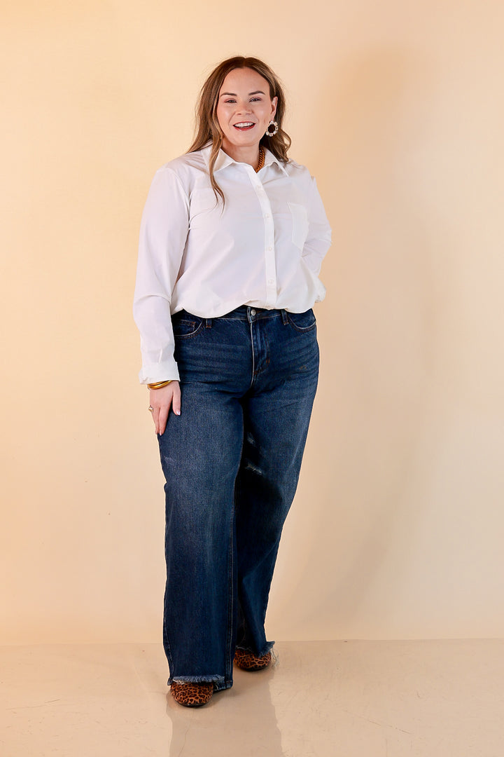 A woman in a white button-up shirt and dark wash Judy Blue baggy jeans with a frayed hem and leopard flats