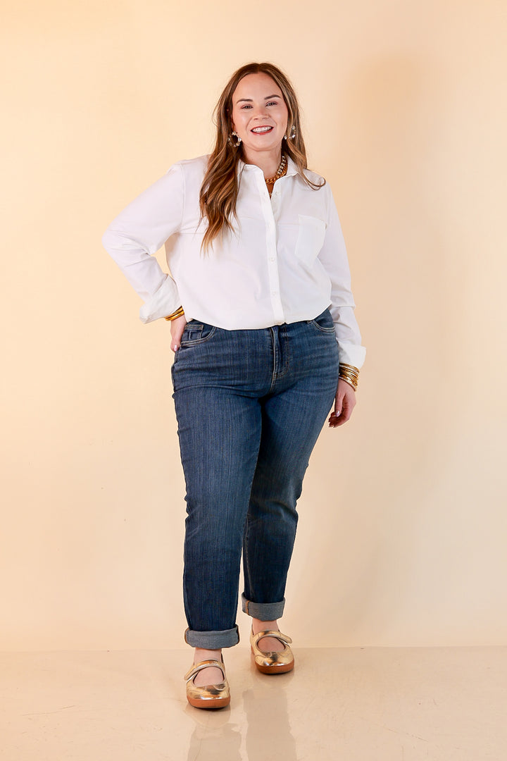 A woman in a white button-up shirt and medium wash Judy Blue cuffed boyfriend jeans with gold bangles and metallic gold flats