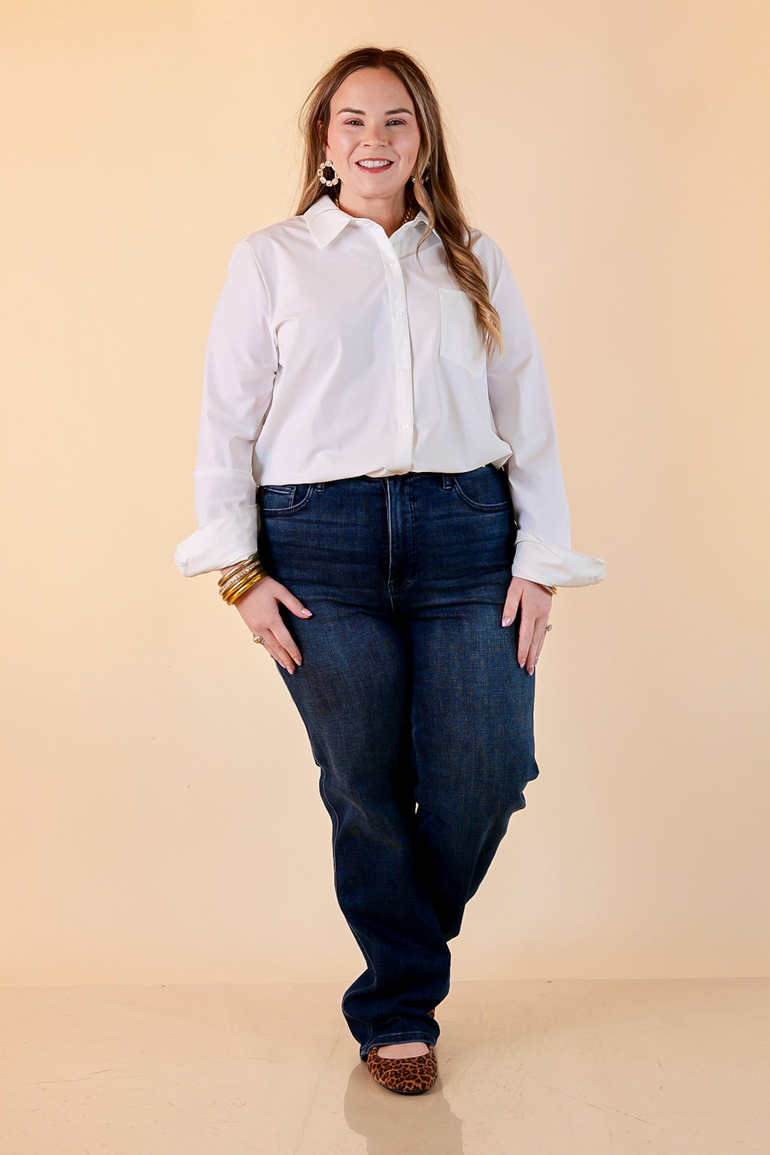 A woman in a white button-up shirt and dark wash Judy Blue tummy control straight leg jeans with gold bangles and leopard flats